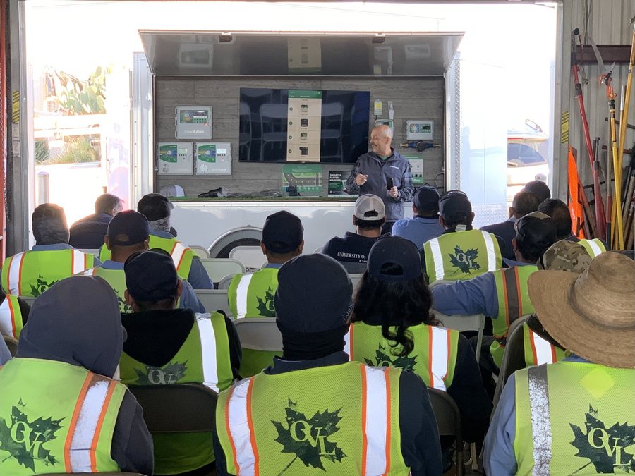 Ed Perez leading irrigation controller training for a seated crew in high-visibility vests at a company yard